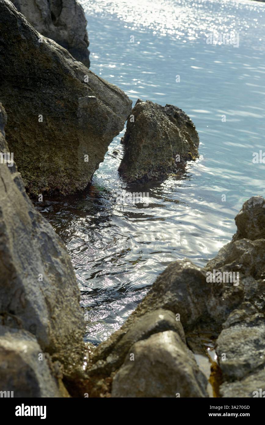 Costa rocciosa con luce solare che si riflette sulla tranquilla superficie dell'oceano. Hydra, Grecia Foto Stock