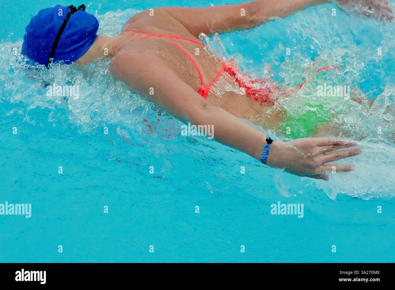 Nuotatore di triathlon in costume da bagno colorato che scivola attraverso una piscina blu brillante, indossando un berretto blu. Foto Stock