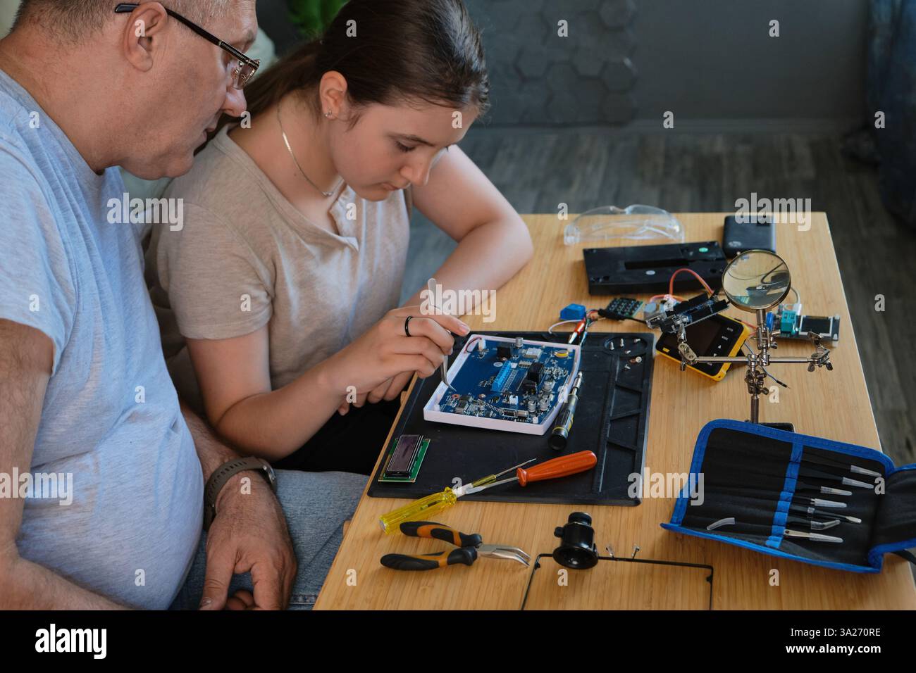 Nonno e nipote lavorano insieme a un progetto di elettronica a un tavolo. Ideale per famiglie, istruzione e fai da te Foto Stock