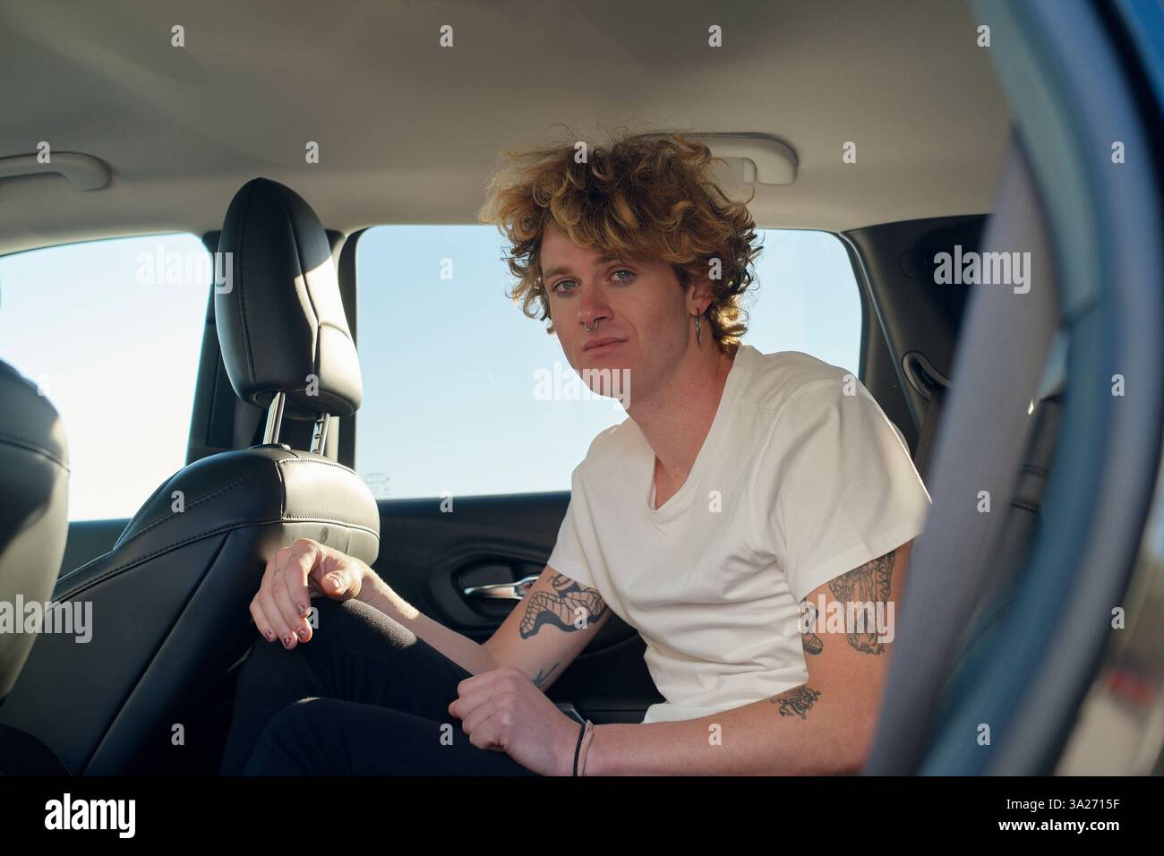 Uomo con capelli ricci seduto sul sedile posteriore di un'auto che guarda fuori dal finestrino con un'espressione neutra. Miami, Florida, Stati Uniti Foto Stock