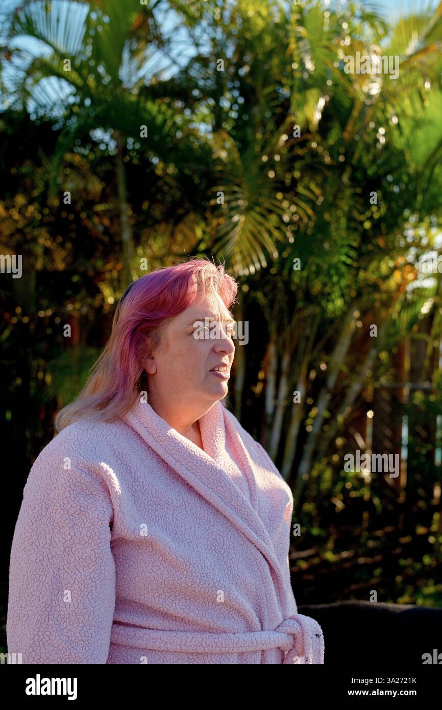 Donna con i capelli rosa in una veste all'aperto, circondata da lussureggianti piante verdi. California, Stati Uniti Foto Stock