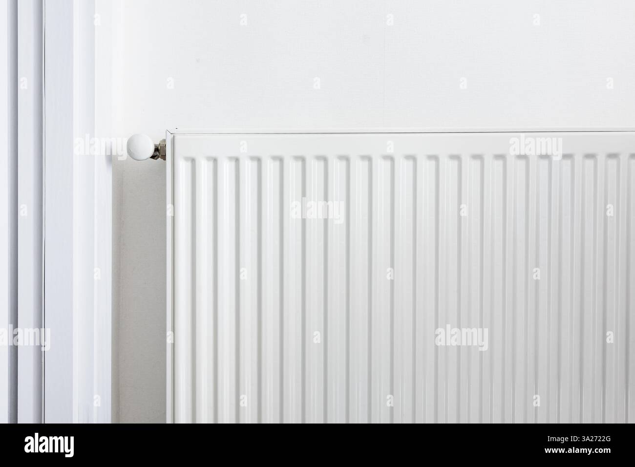 Primo piano di un radiatore in metallo bianco con una valvola di controllo della temperatura. Moderno sistema di riscaldamento domestico, concetto di efficienza energetica. Interni minimalisti con Foto Stock