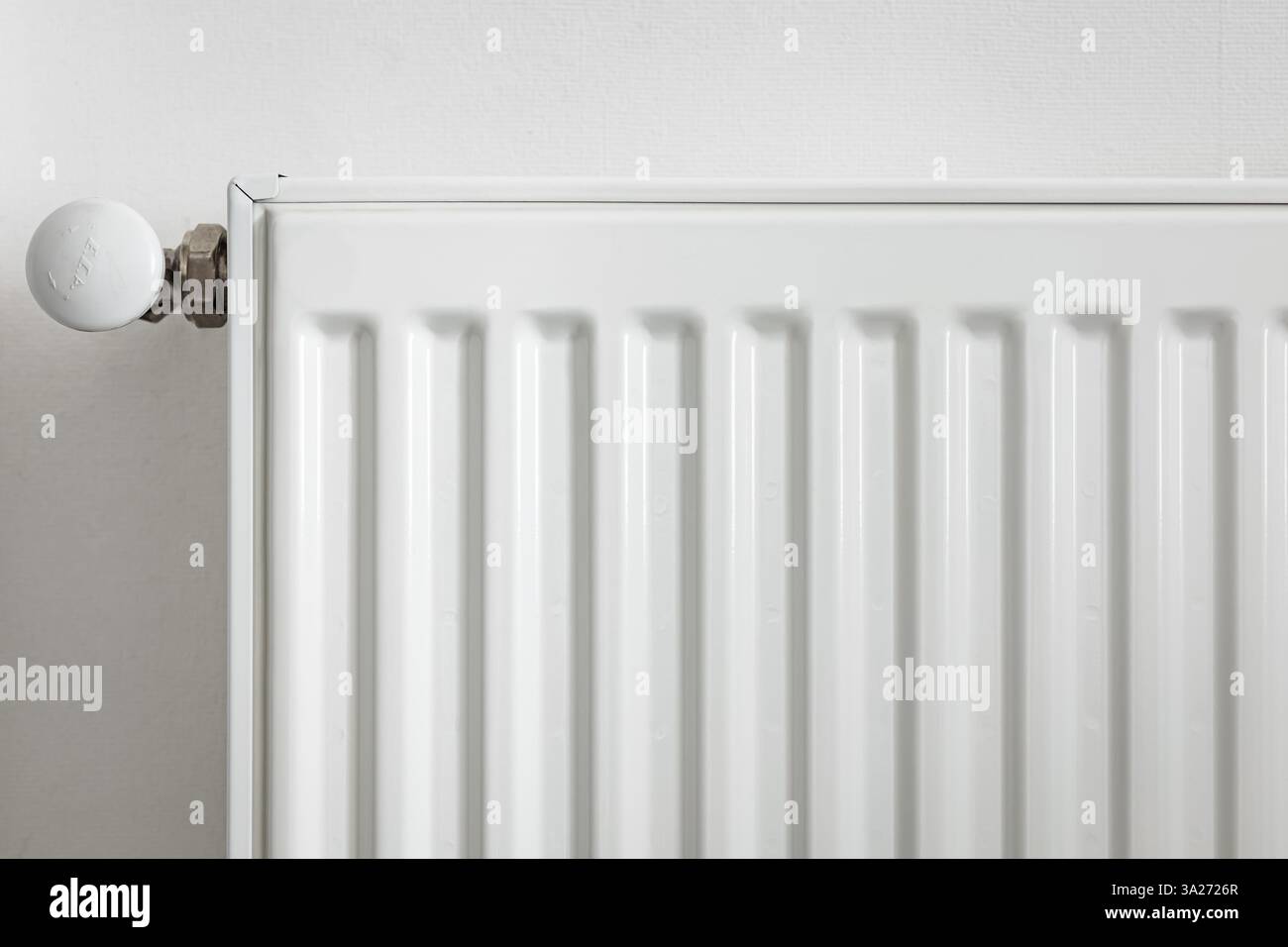 Primo piano di un radiatore in metallo bianco con una valvola di controllo della temperatura. Moderno sistema di riscaldamento domestico, concetto di efficienza energetica. Interni minimalisti con Foto Stock