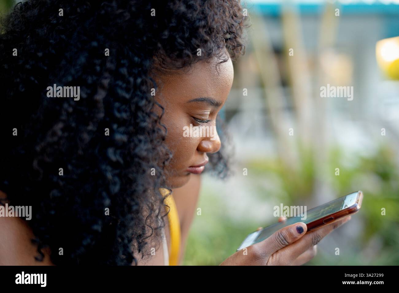 Donna con capelli ricci che si concentra con attenzione sul suo smartphone all'aperto. Miami, Florida, Stati Uniti Foto Stock