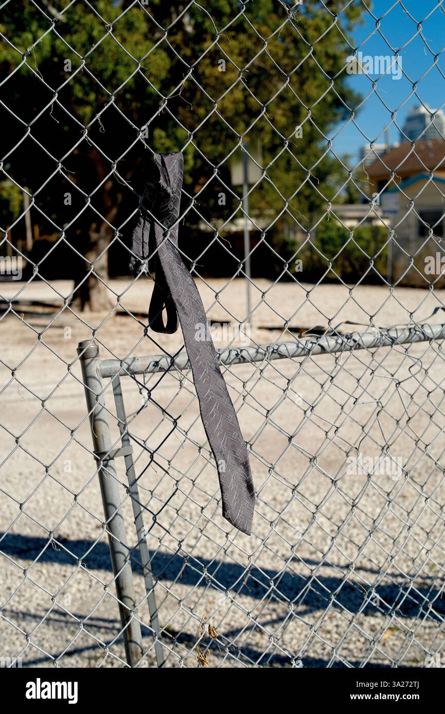 Una cravatta nera è appesa a una recinzione metallica con maglie a catena in un ambiente soleggiato all'aperto. Miami, Florida, Stati Uniti Foto Stock
