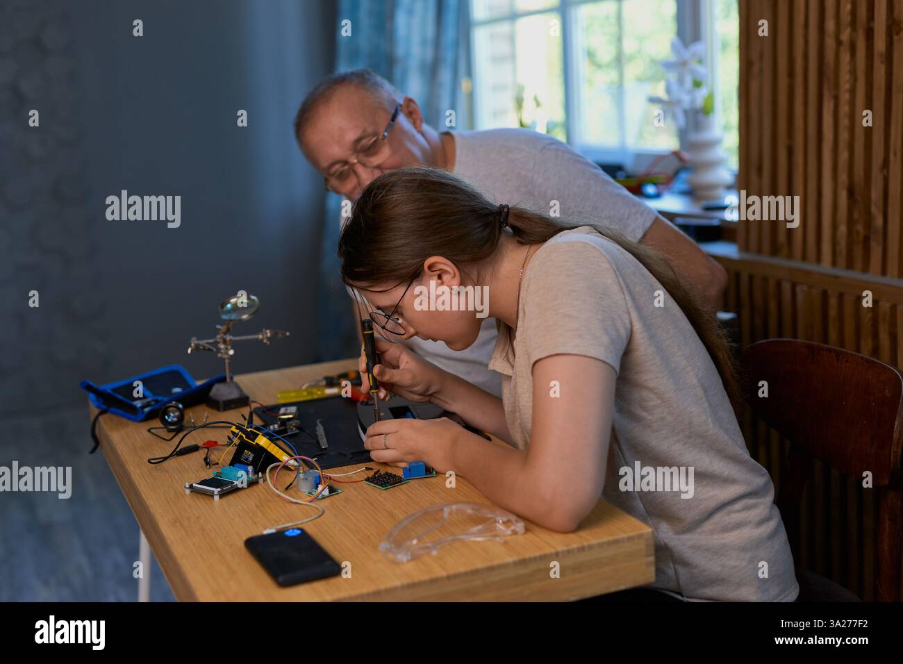 Nonno e nipote lavorano insieme a un progetto di elettronica a un tavolo. Ideale per famiglie, istruzione e fai da te Foto Stock