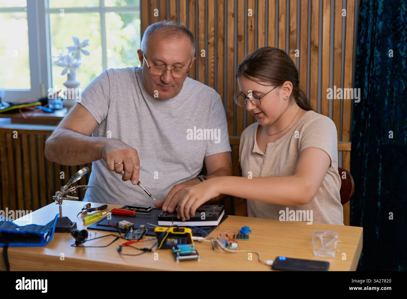 Nonno e nipote lavorano insieme a un progetto di elettronica a un tavolo. Ideale per famiglie, istruzione e fai da te Foto Stock