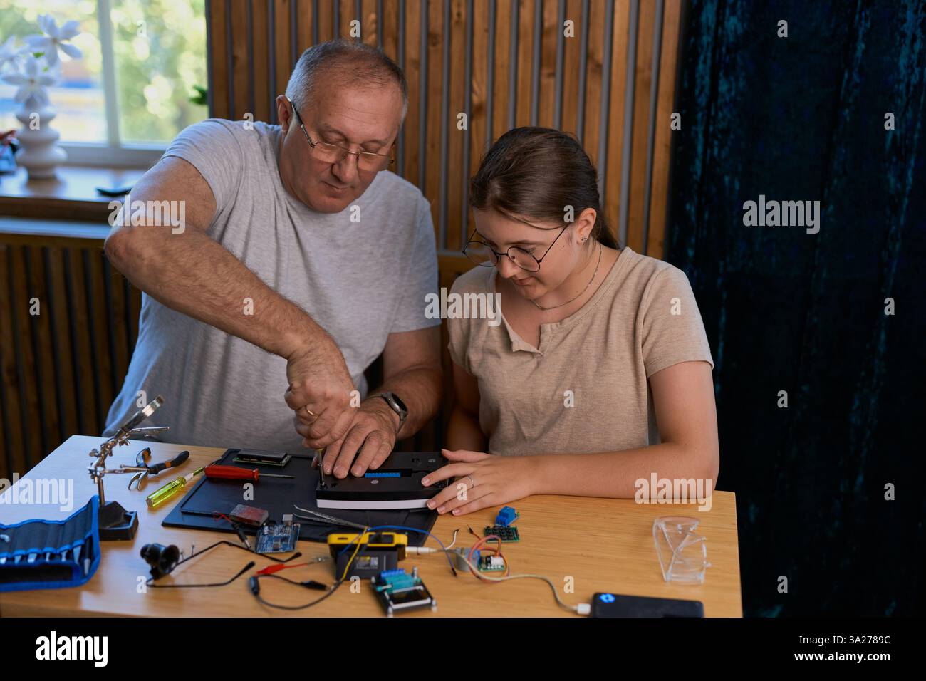 Nonno e nipote lavorano insieme a un progetto di elettronica a un tavolo. Ideale per famiglie, istruzione e fai da te Foto Stock