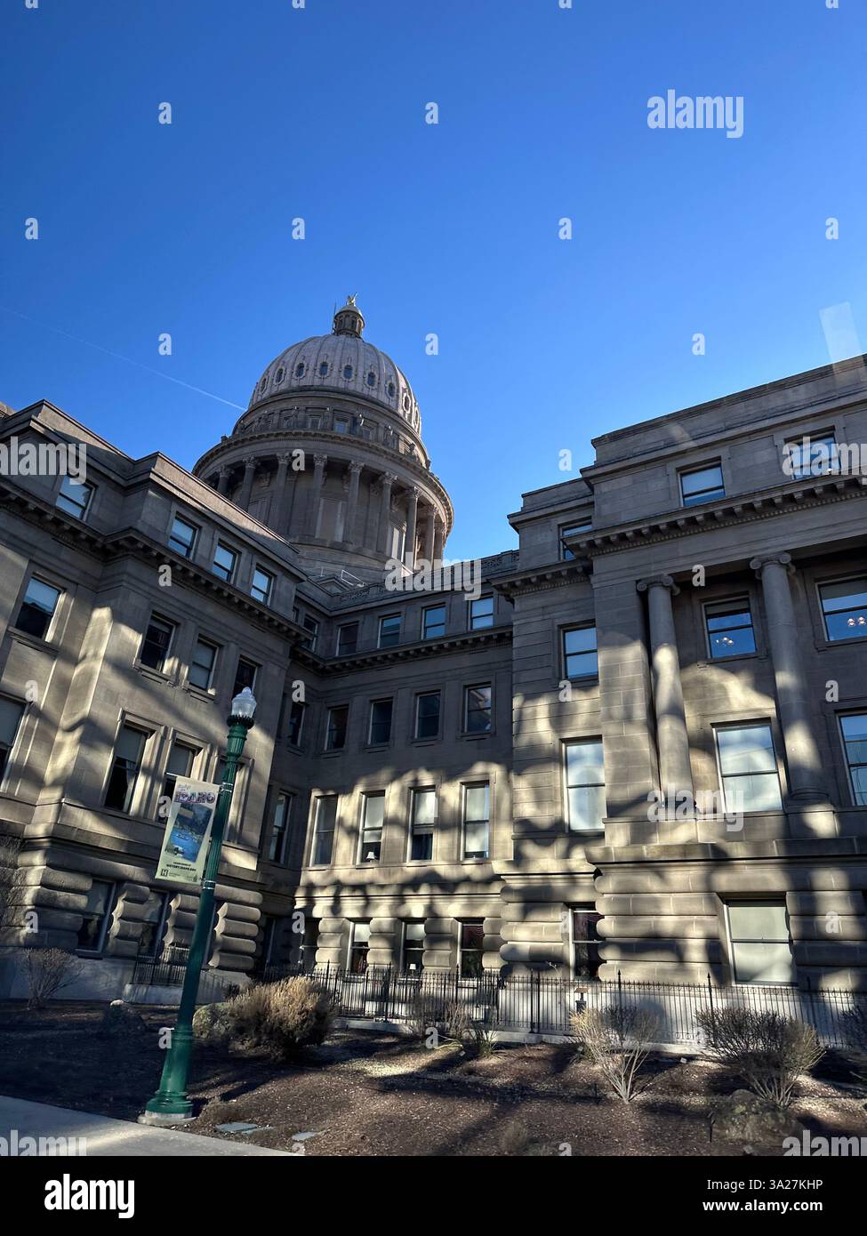 Un maestoso palazzo del governo con una cupola prominente si erge sotto un cielo azzurro limpido che getta ombre sulla sua facciata in pietra. - Immagine stock catturata con smartphone