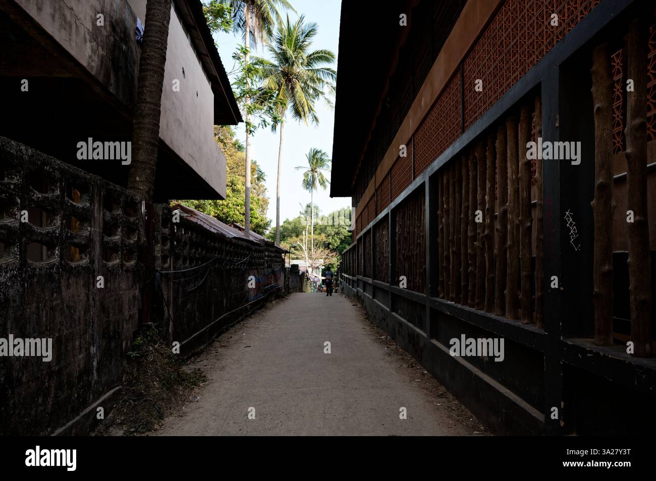 Vicolo tranquillo fiancheggiato da rustici edifici in legno e cemento, che conducono verso il verde tropicale a Railay Foto Stock