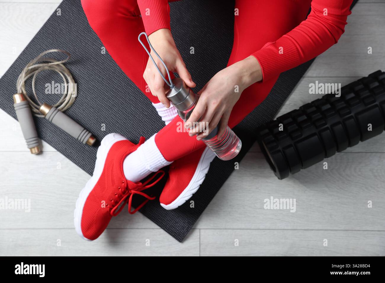Donna con bottiglia d'acqua e attrezzature da palestra al piano, vista dall'alto Foto Stock