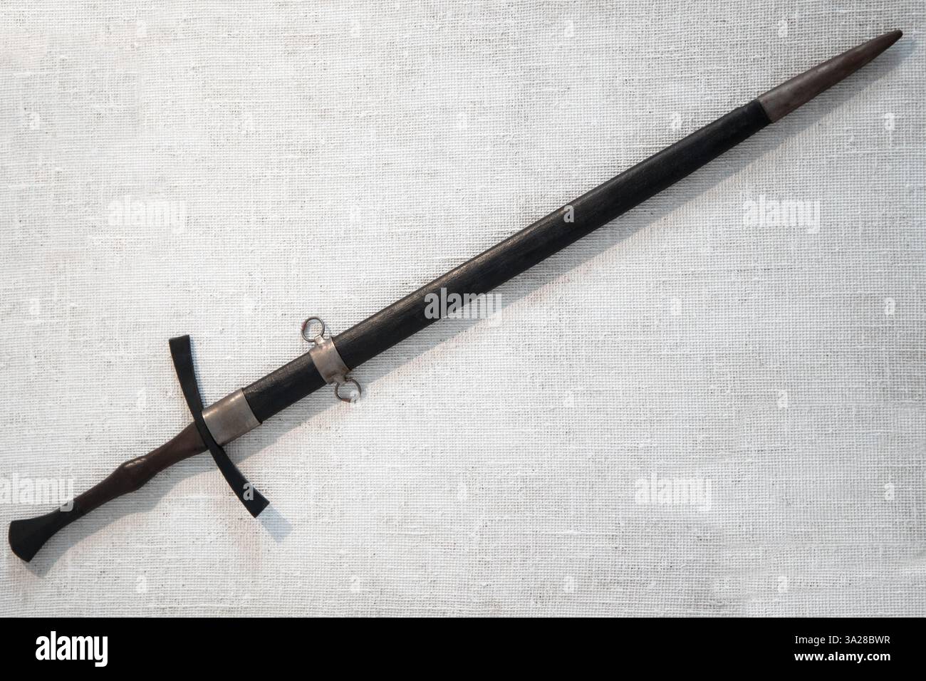 Una vista dettagliata di una storica spada medievale racchiusa in una sciabola, adagiata su una superficie in tela di lino testurizzata, esemplificando l'artigianato e l'histo Foto Stock