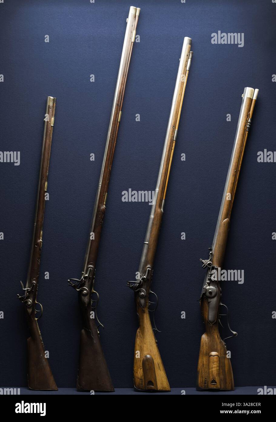 Una linea di fucili antichi a pietra focaia, che mostrano il design storico delle armi da fuoco, collocati su uno sfondo blu Foto Stock