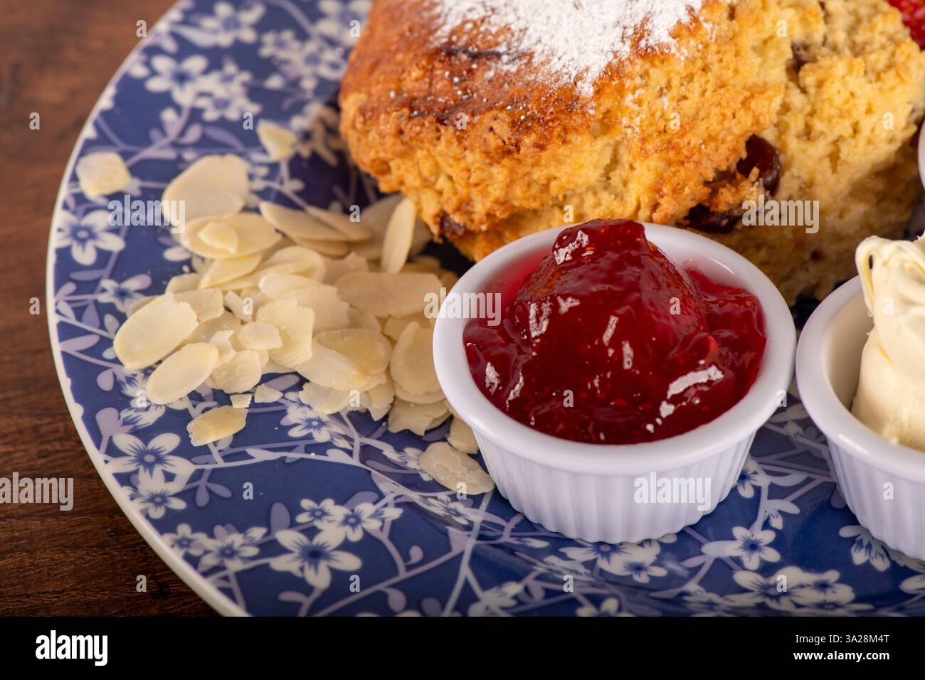 Uno Scone di mandorle di ciliegia con marmellata di fragole . La gelatina si trova in una ciotola bianca di panna coagulata Foto Stock