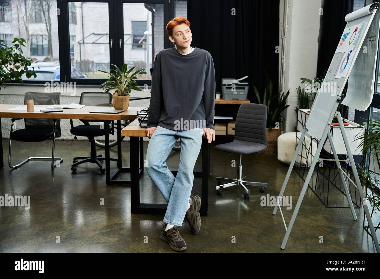 Giovane uomo dedicato con i capelli rossi si impegna in un lavoro attento in uno spazio ufficio contemporaneo. Foto Stock