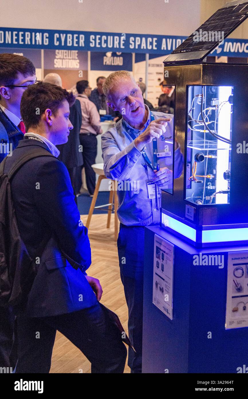 Un addetto alle vendite che mostra e mostra una mostra a due clienti per Glenair allo Space Comm Expo 2025 presso l'Excel Centre di Londra, Regno Unito Foto Stock