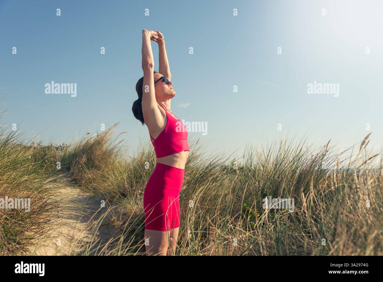 donna sportiva con le braccia alzate in piedi su dune di sabbia Foto Stock