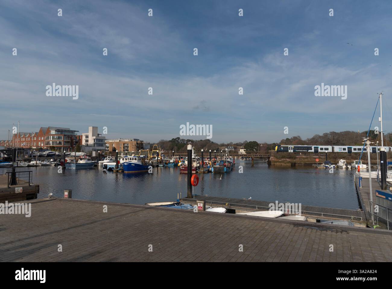 Lymington Harbour Hampshire Inghilterra Regno Unito. 10.03.2025. Battelli da pesca sugli ormeggi a pelo e il treno passeggeri della South West Railways passa per Brockenhurst Foto Stock