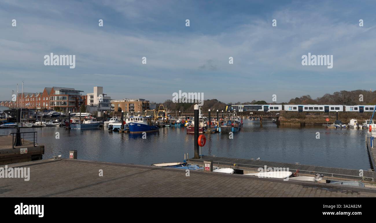 Lymington Harbour Hampshire Inghilterra Regno Unito. 10.03.2025. Battelli da pesca sugli ormeggi a pelo e il treno passeggeri della South West Railways passa per Brockenhurst Foto Stock