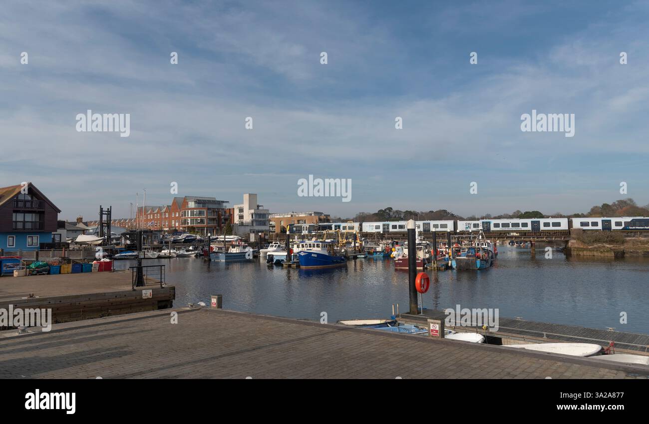Lymington Harbour Hampshire Inghilterra Regno Unito. 10.03.2025. Battelli da pesca sugli ormeggi a pelo e il treno passeggeri della South West Railways passa per Brockenhurst Foto Stock