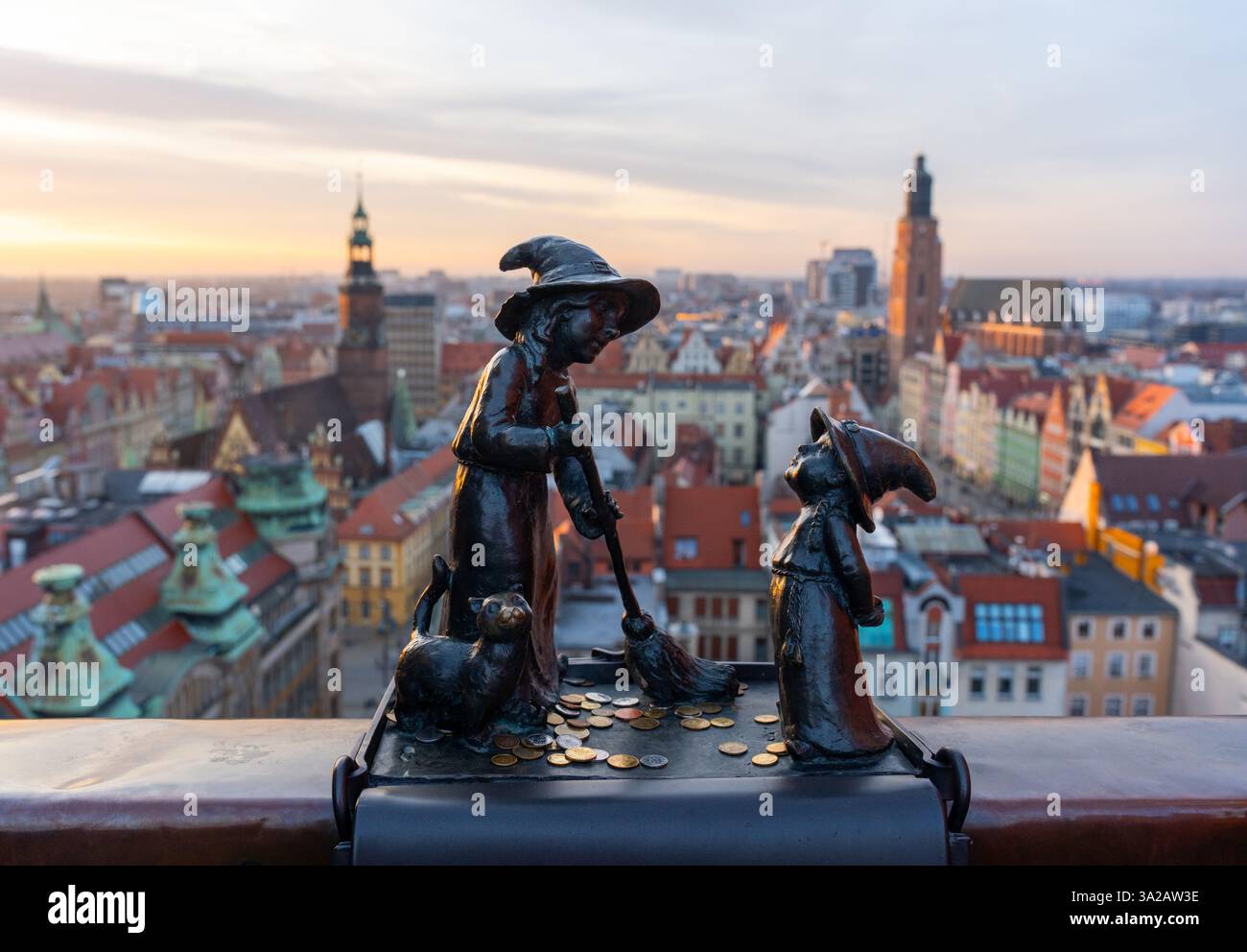 15.01.2025 Breslavia, Polonia. Affascinanti sculture in bronzo di piccole streghe con gatto sul tetto di Breslavia, con lo splendido skyline della città vecchia al tramonto. Trav Foto Stock
