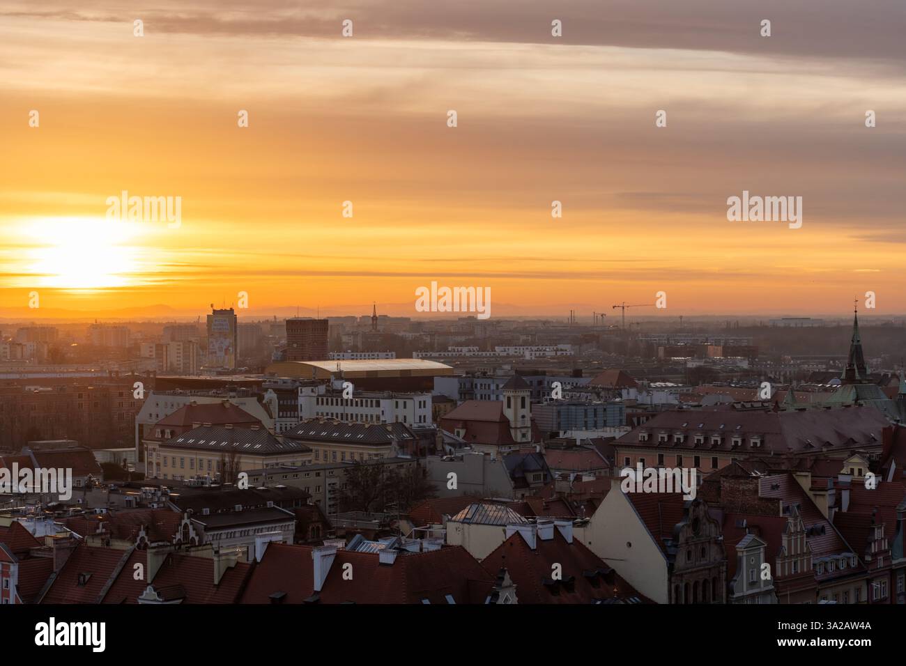 Tramonto mozzafiato sullo skyline della città europea con tetti storici, calde tonalità dorate e montagne lontane all'orizzonte. Foto di alta qualità Foto Stock