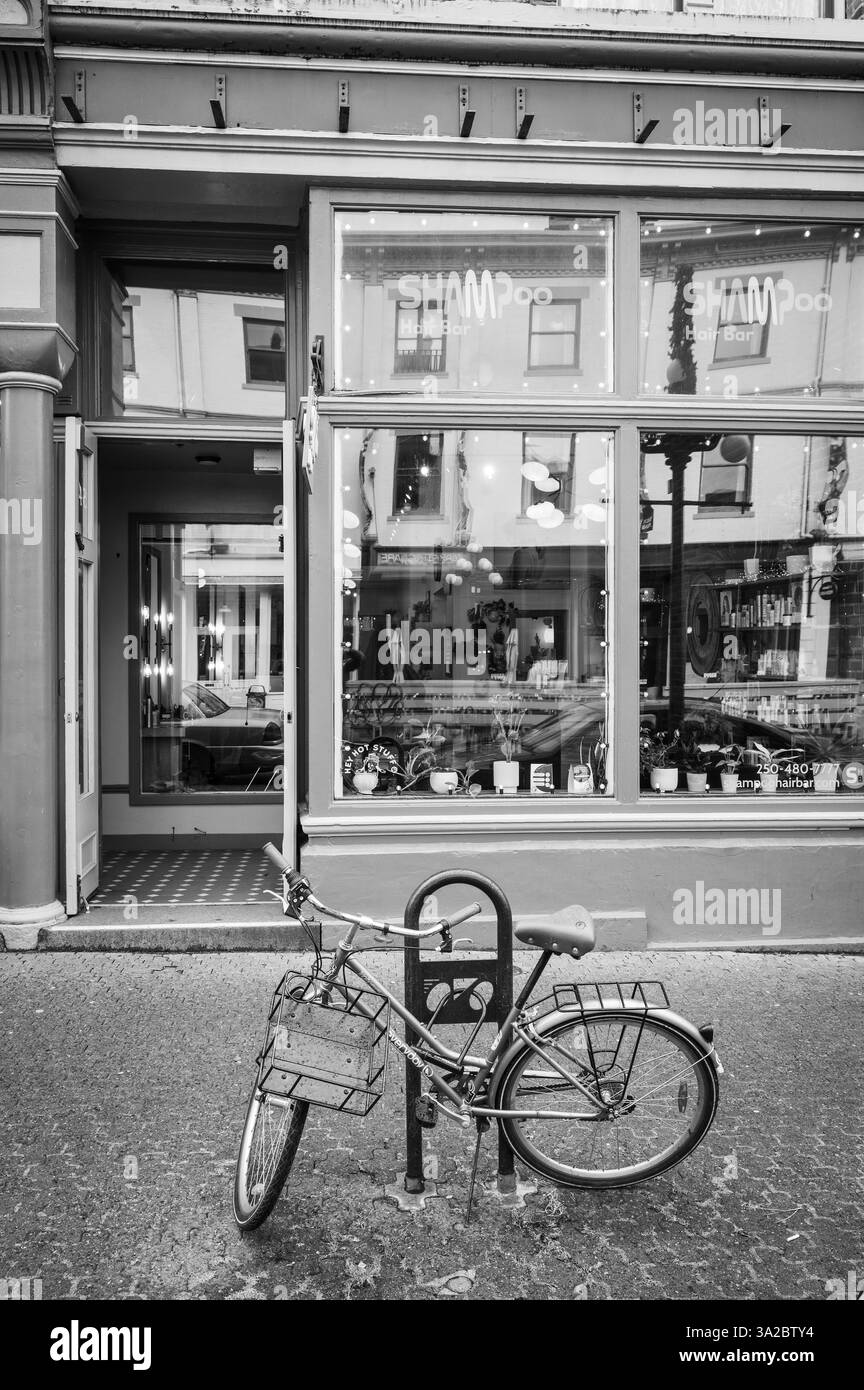 Una bicicletta chiusa vicino ai colorati negozi di epoca vittoriana lungo Johnson Street nel centro di Victoria BC, Canada. Immagine in bianco e nero. Foto Stock
