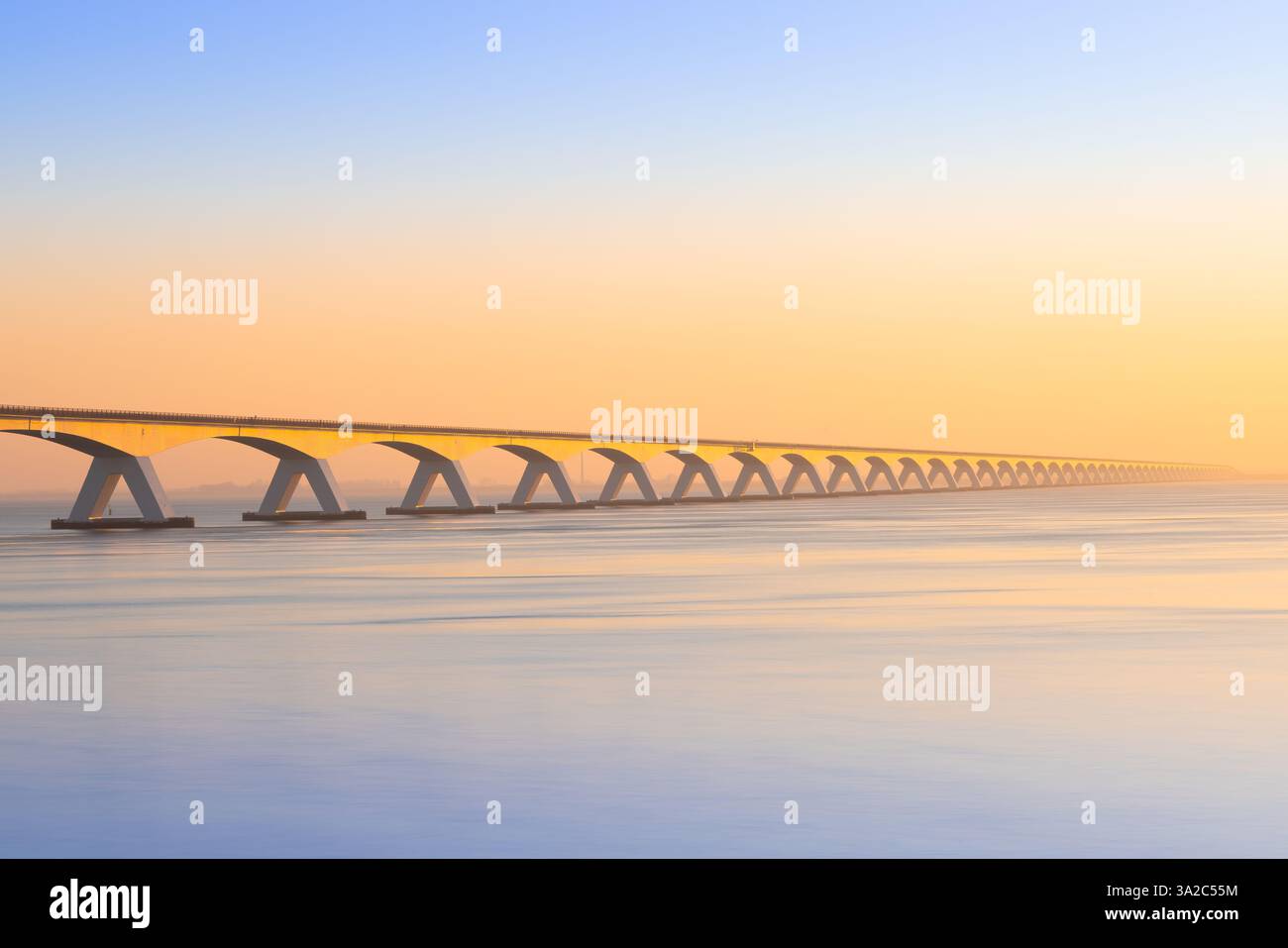 Luce dorata sullo Zeelandbrug in Zelanda al crepuscolo con riflessi sull'acqua: Un'immagine di paesaggio Foto Stock