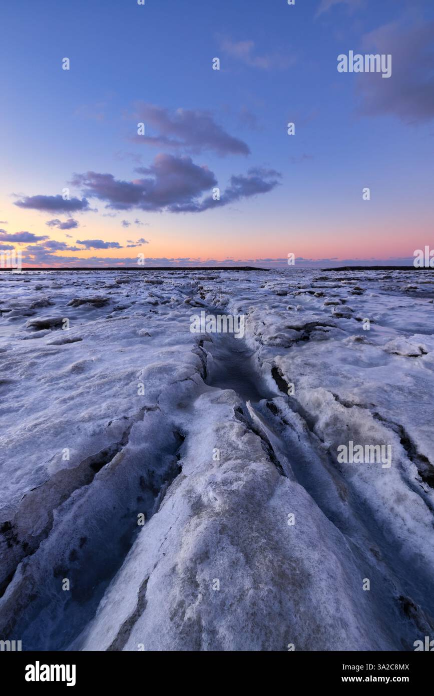 Un paesaggio invernale ghiacciato del Waddenzee nei Paesi Bassi con piattaforme ghiacciate e linee principali e un bel cielo - un freddo paesaggio invernale Foto Stock
