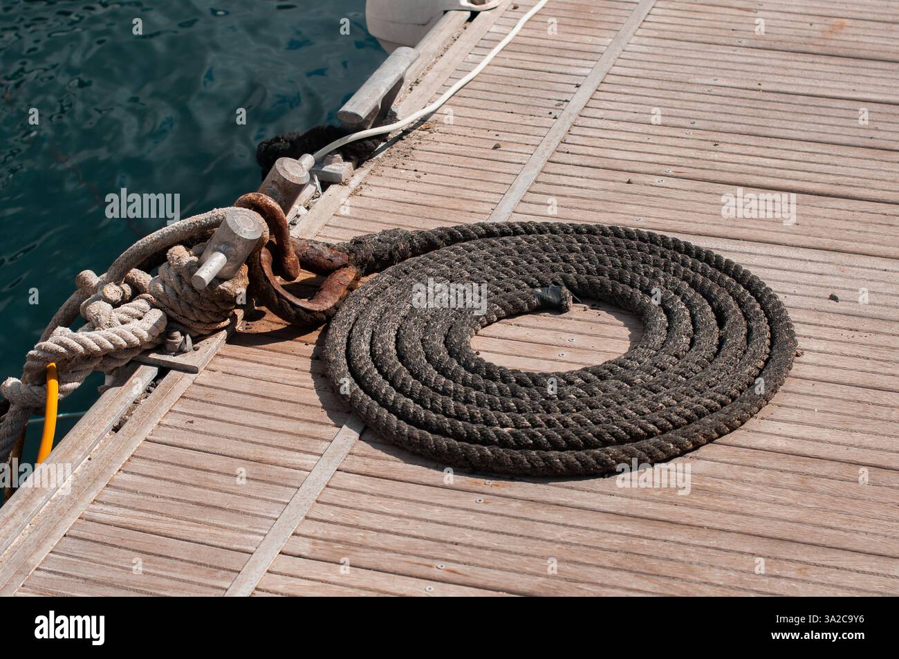 Fune nera arrotolata su banchina di legno vicino all'acqua con tacchetti in metallo arrugginito Foto Stock Fune nera arrotolata su banchina di legno vicino all'acqua con tacchetti in metallo arrugginito Foto Stock