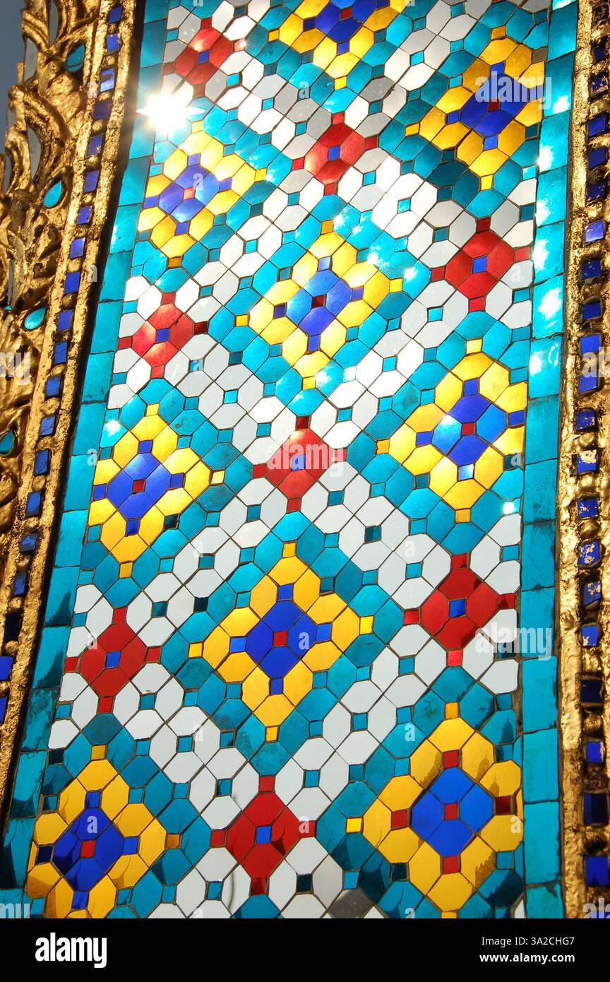 Un primo piano di una vibrante parete a mosaico al Grand Palace di Bangkok, Thailandia, caratterizzato da intricati motivi geometrici in blu, oro, rosso e bianco Foto Stock