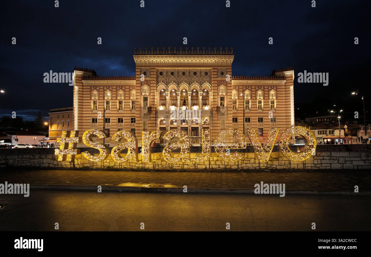 Testo illuminato #SARAJEVO di fronte al municipio di notte in Bosnia ed Erzegovina Foto Stock