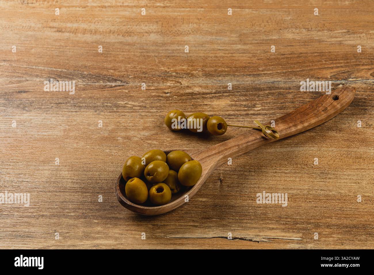 Le olive verdi fresche riposano in un cucchiaio di legno su una superficie di legno intemprata, che mostra il loro colore ricco e la consistenza liscia, mentre mettono in risalto una l naturale Foto Stock