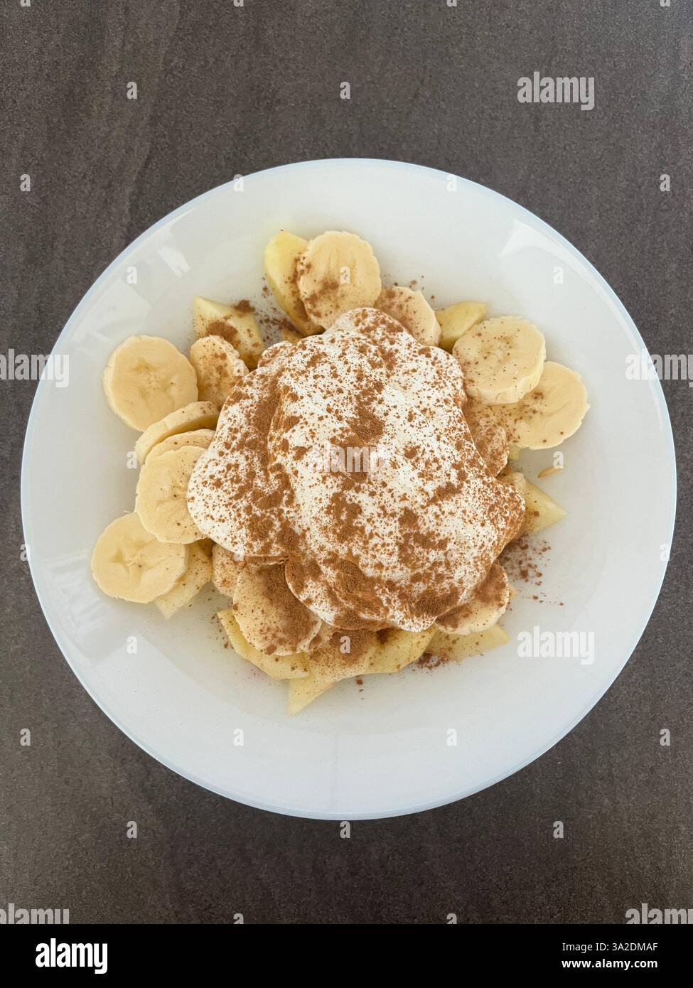 Uno spuntino salutare con banane e mele fresche, abbinato a cremoso yogurt greco e una spolverata di cannella per un sapore extra. Foto Stock