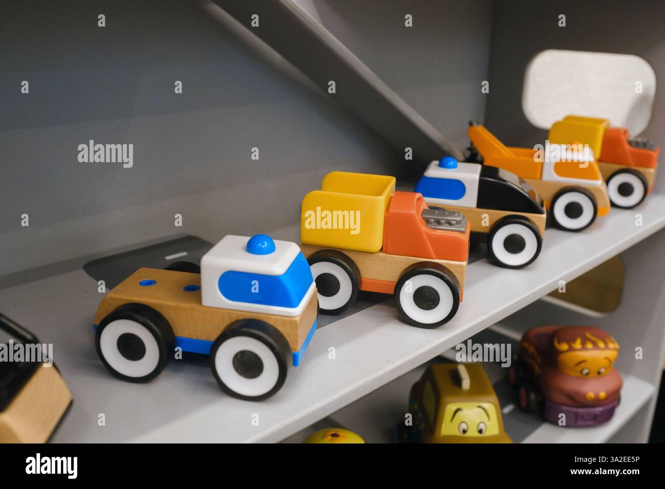 Una collezione di vivaci macchinine e camion giocattolo in legno è esposta su un robusto scaffale grigio in una allegra sala giochi, invitando i bambini a impegnarsi in un creativo Foto Stock