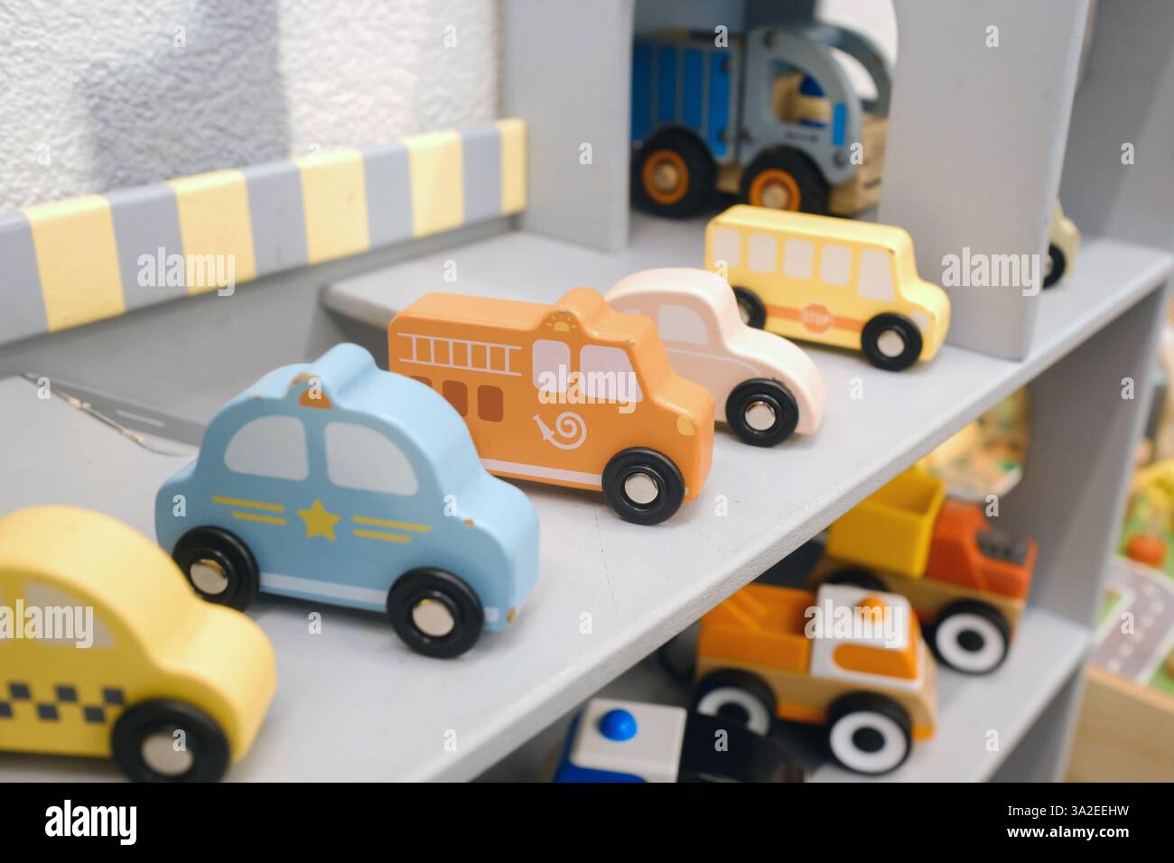 Una collezione di vivaci macchinine e camion giocattolo in legno è esposta su un robusto scaffale grigio in una allegra sala giochi, invitando i bambini a impegnarsi in un creativo Foto Stock