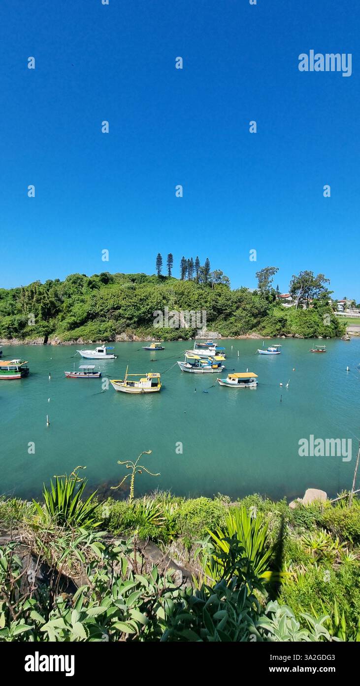 Una splendida scena costiera con vibranti acque turchesi, lussureggianti isole verdi e una serie di barche colorate che galleggiano dolcemente sul mare calmo - Immagine stock catturata con smartphone
