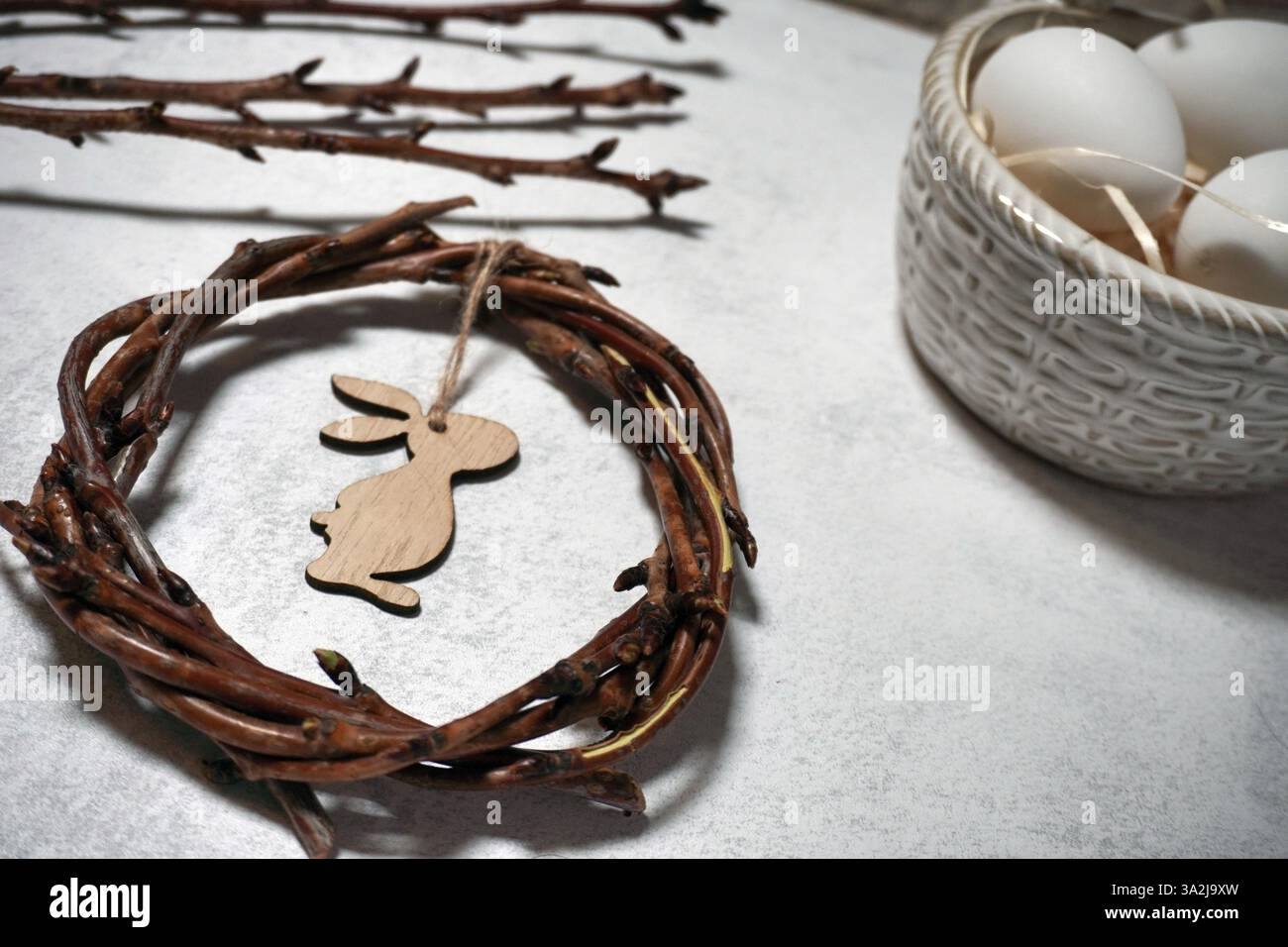 la corona pasquale di rami di vite con coniglio su sfondo grigio con imitazione. rami decorativi con boccioli, salice e uova Foto Stock