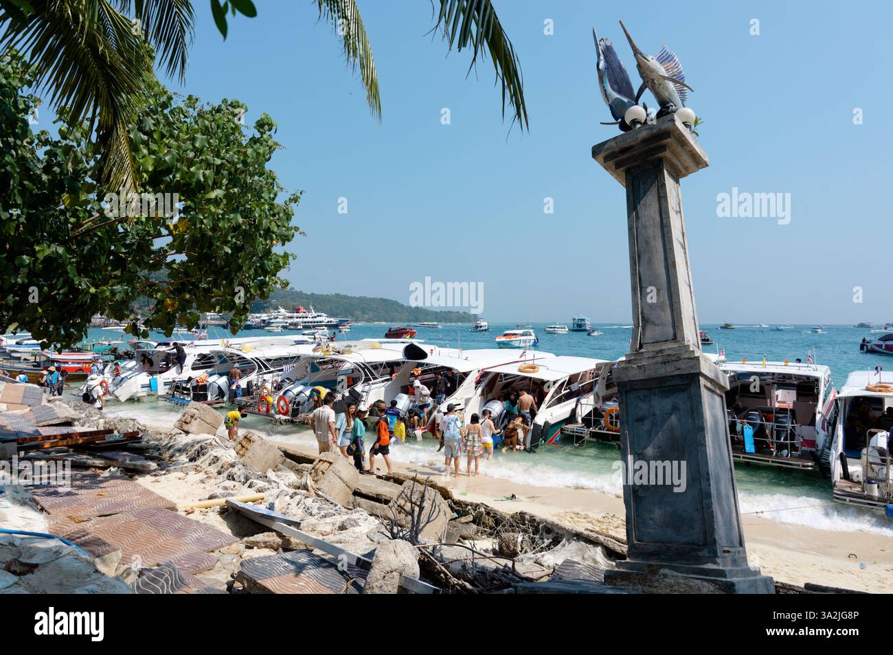 I turisti arrivano a un molo affollato sulle isole Phi Phi, mentre i motoscafi costeggiano la costa Foto Stock
