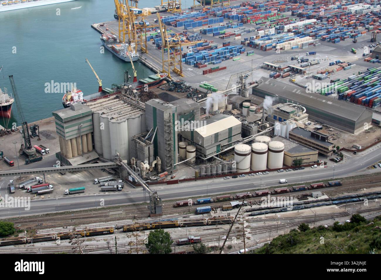 Porto affollato con navi da carico e un grande complesso industriale. Vista ad alto angolo, operazioni logistiche e colori disattivati Foto Stock
