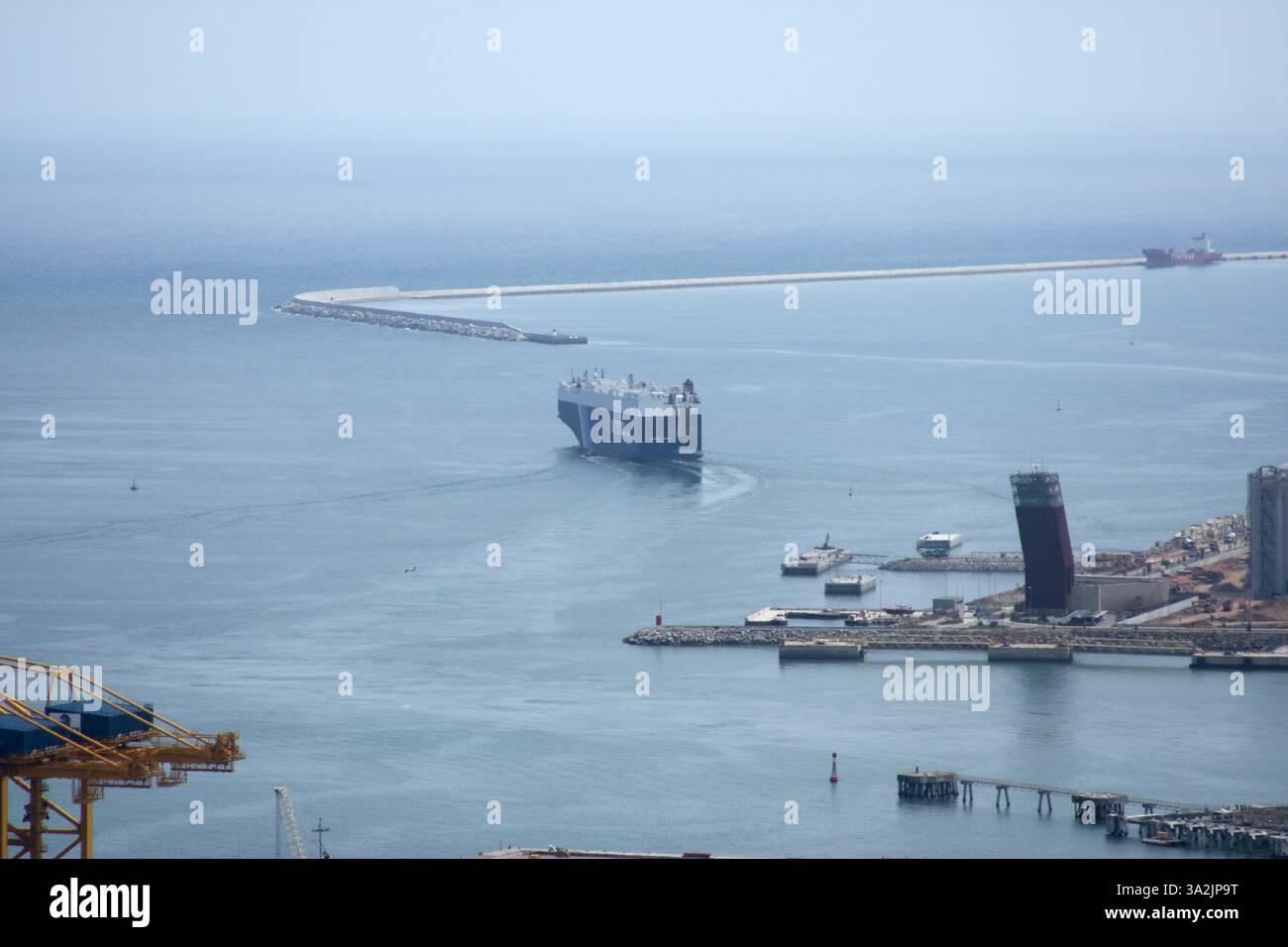 Frangiflutti lunghi e angolari che si estendono in mare con una nave da carico che passa. Prospettiva aerea, infrastrutture portuali e atmosfera nebulosa Foto Stock