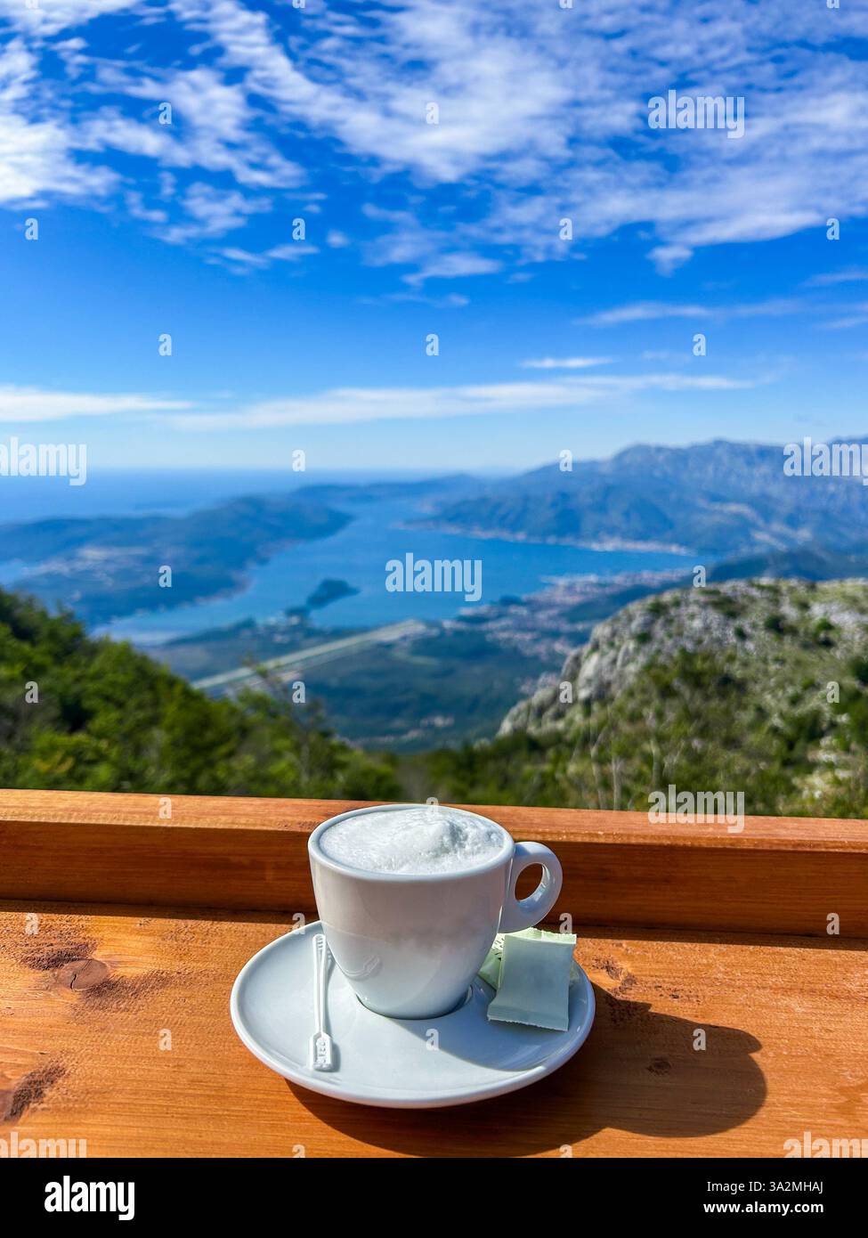Una tazza di cappuccino fumante gustata con una vista mozzafiato su Cattaro e la baia di Cattaro. Una miscela perfetta di sapori ricchi e bellezza naturale. Foto Stock
