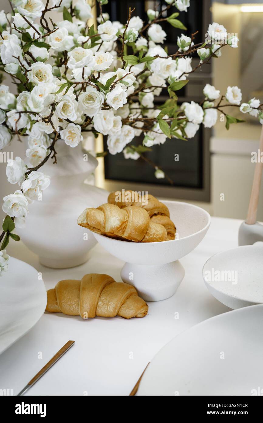 Colazione elegante con croissant in una cucina bianca con fiori Foto Stock