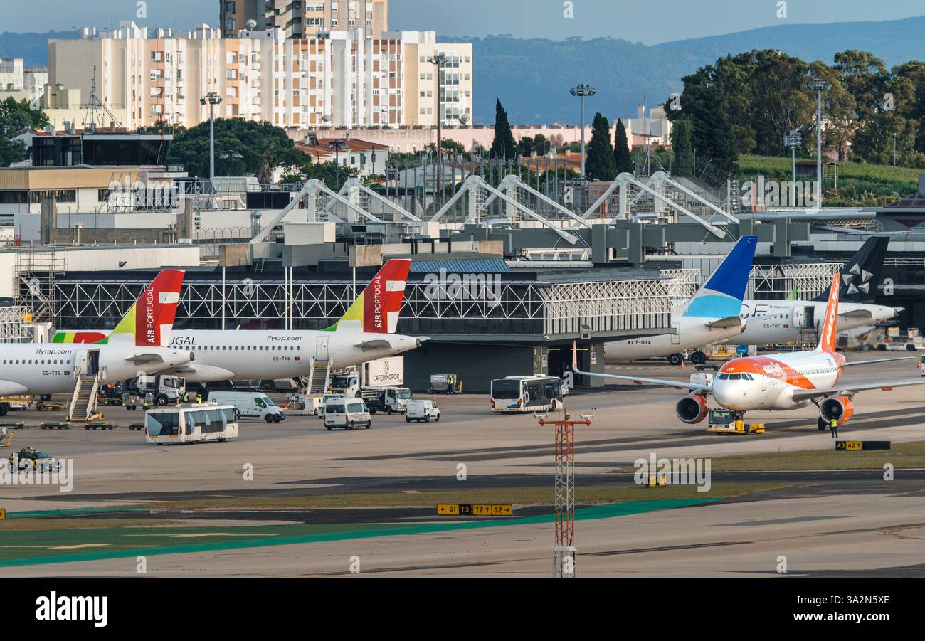 Lisbona, Portogallo - 24 aprile 2024: Aerei TAP, ASL Airlines e EasyJet all'aeroporto di Lisbona pronti per l'imbarco e il decollo in una giornata di sole, cielo azzurro. Veicoli di supporto a terra e infrastruttura del terminal 1 dell'aeroporto, edifici cittadini in background. Foto Stock