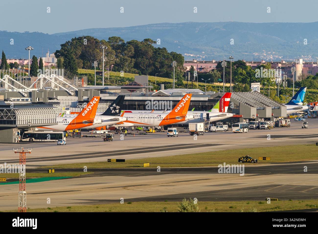 Lisbona, Portogallo - 24 aprile 2024: Gli aerei TAP, Azores Airlines e EasyJet all'aeroporto di Lisbona sono pronti per l'imbarco e il decollo in una giornata di sole, cielo azzurro. Veicoli di supporto a terra, infrastruttura del terminal 1 dell'aeroporto, edifici cittadini in background. Foto Stock