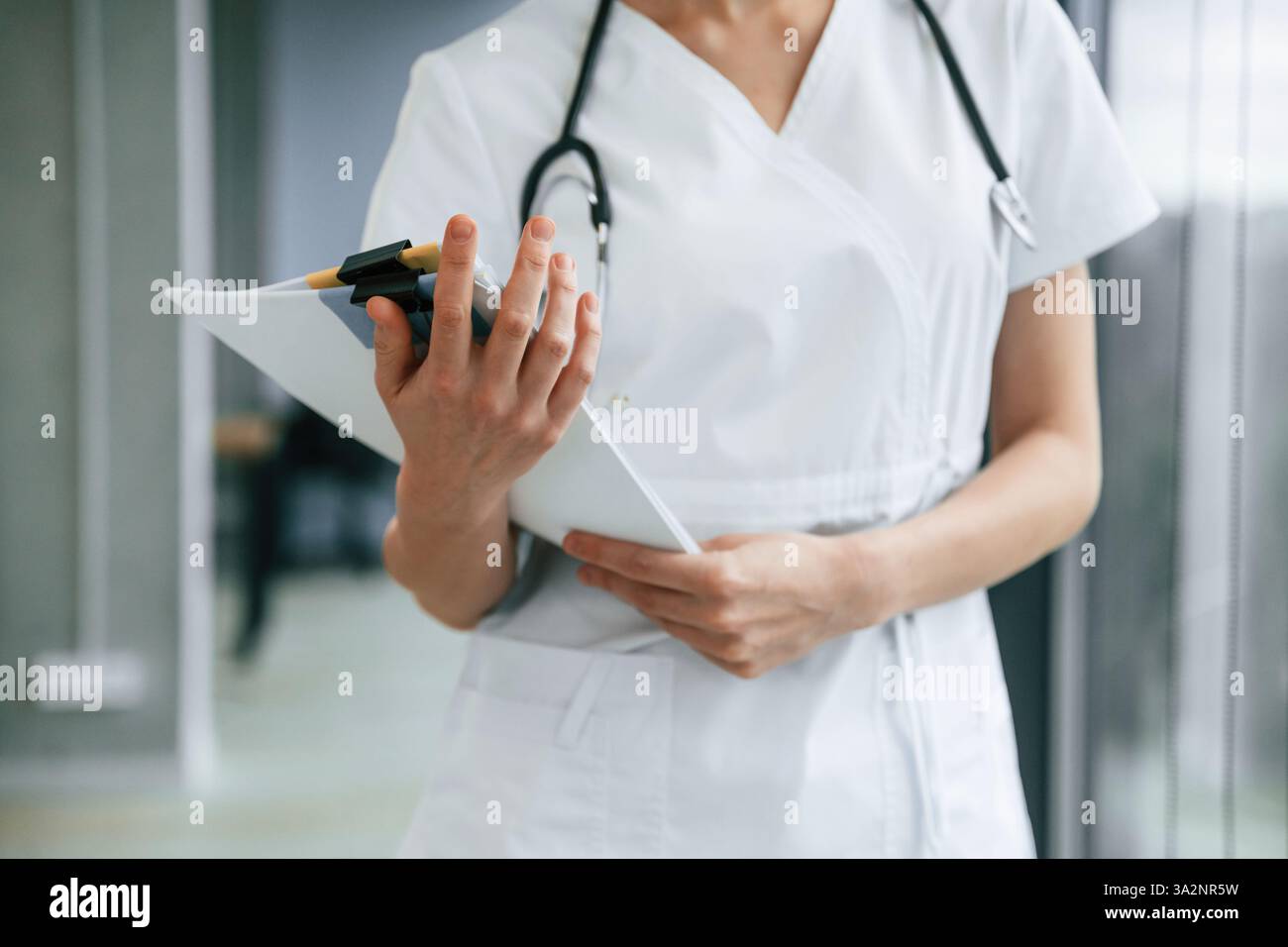 Stare in piedi e tenere in mano i documenti. Medico donna in giacca bianca è al chiuso. Foto Stock
