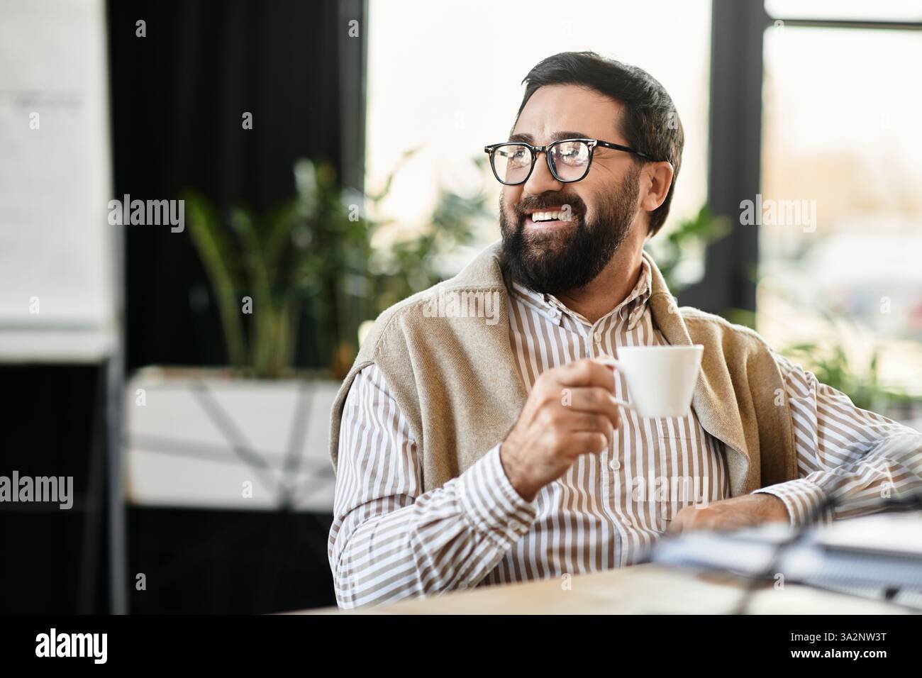Un uomo anziano allegro si rilassa in una caffetteria luminosa, sorseggiando un caffè e assaporando il momento. Foto Stock