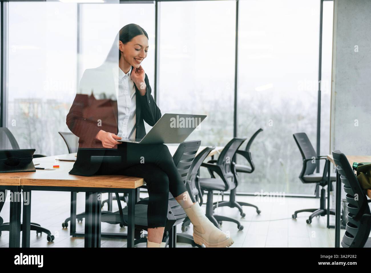 Seduti sul tavolo con il laptop in ginocchio. Una donna d'affari è al chiuso in ufficio. Foto Stock