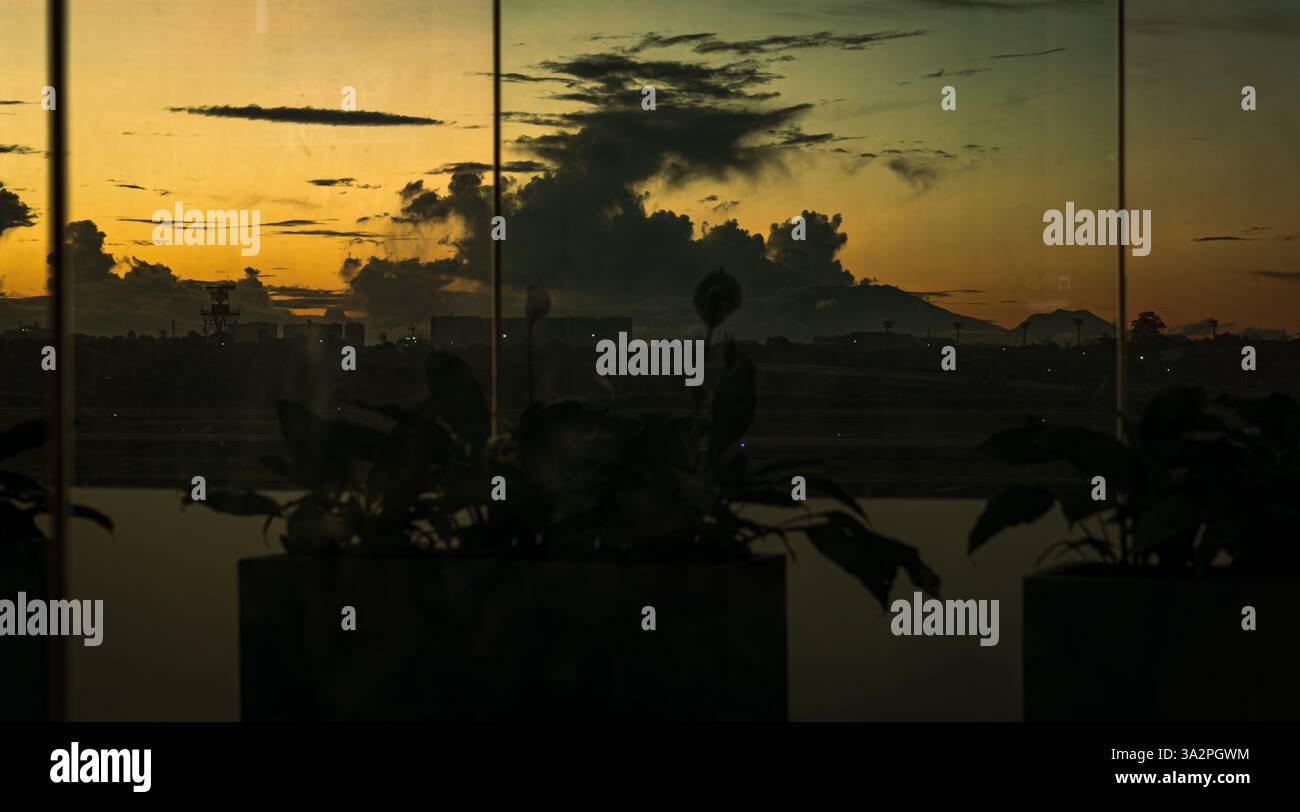 Vista della pista dell'aereo dall'interno della finestra dell'aeroporto, con il tramonto sullo sfondo Foto Stock