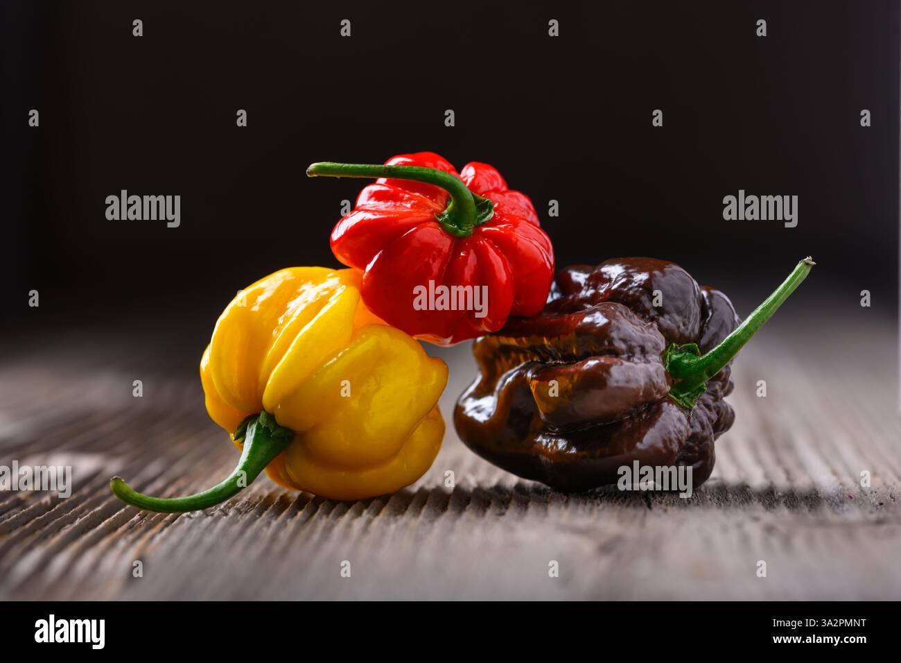 Tre peperoni habanero maturi multicolori (capsicum chinense) su tavola di legno. Peperoni messicani molto caldi. Fotografia gastronomica Foto Stock